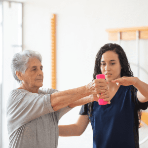 A senior woman working with a Pioneer therapist to improve arm strength using a pink dumbbell. 