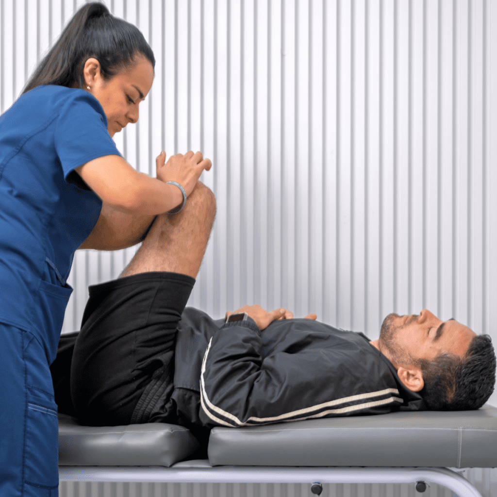 A female therapist in blue scrubs performing a leg stretch on a male patient as part of Pioneer rehabilitation. 