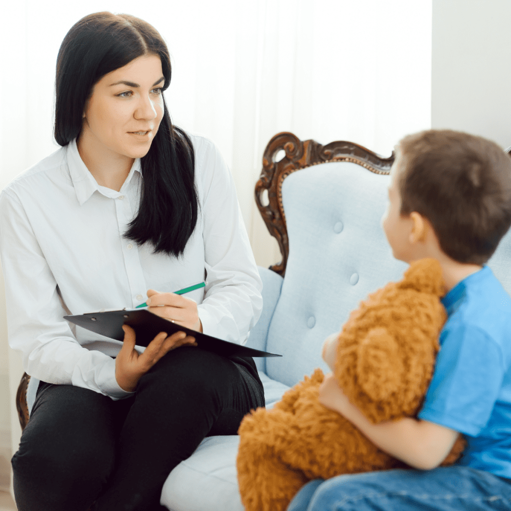 A female psychologist engaging in a supportive consultation with a young child, highlighting the role of behavioral health in pediatric medical outcomes. 