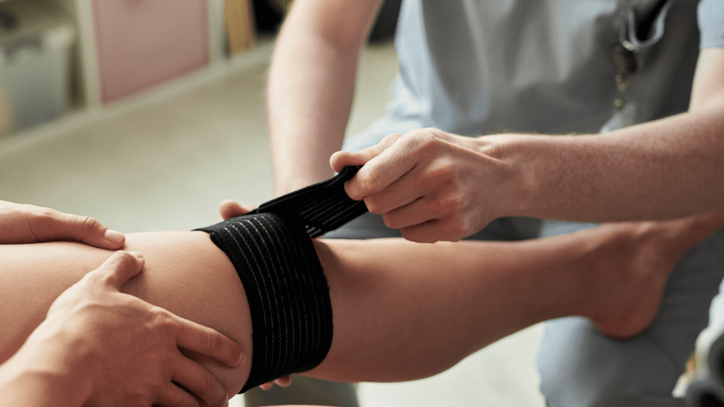 A sports medicine professional wrapping a patient's knee with a black compression bandage to treat an athletic injury.