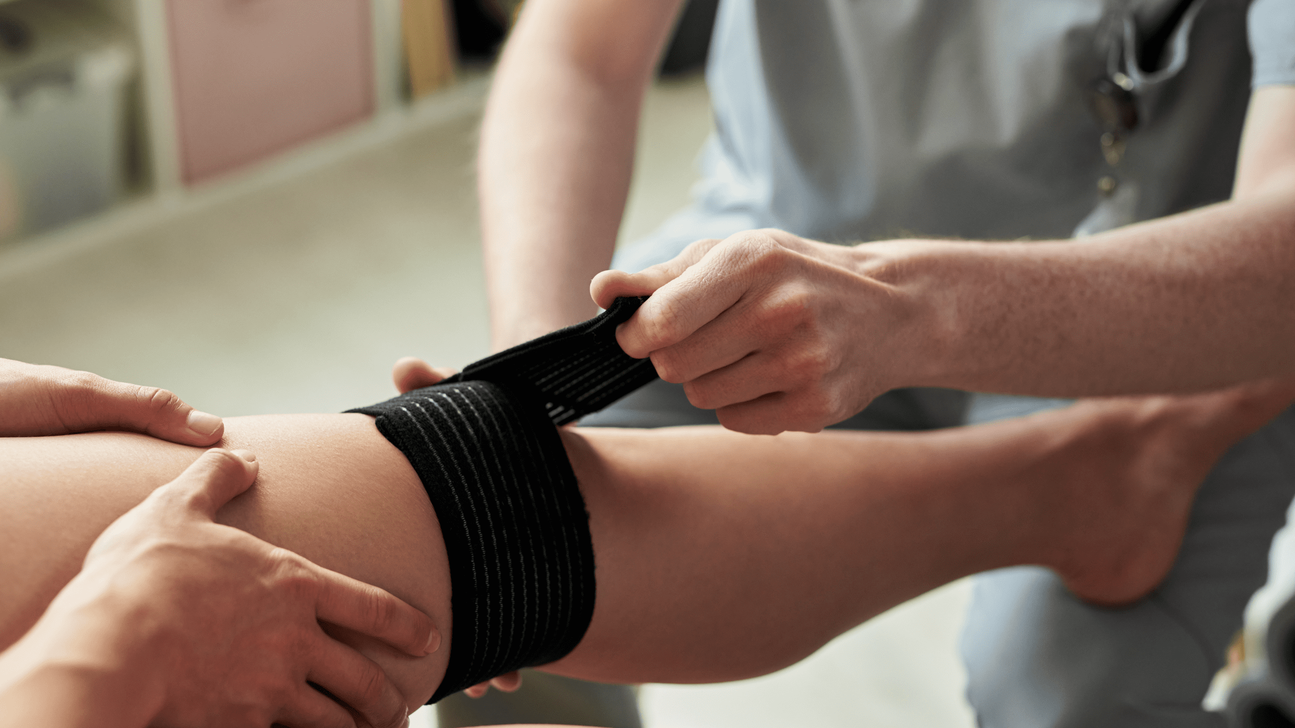 A sports medicine professional wrapping a patient's knee with a black compression bandage to treat an athletic injury.
