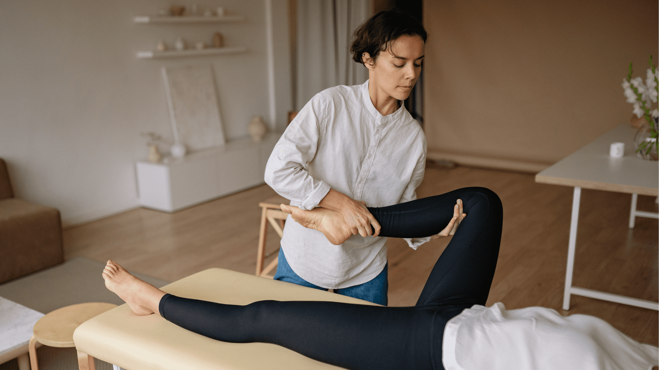 A physical therapist in a white shirt stretching a female patient's leg on a treatment table to increase mobility.