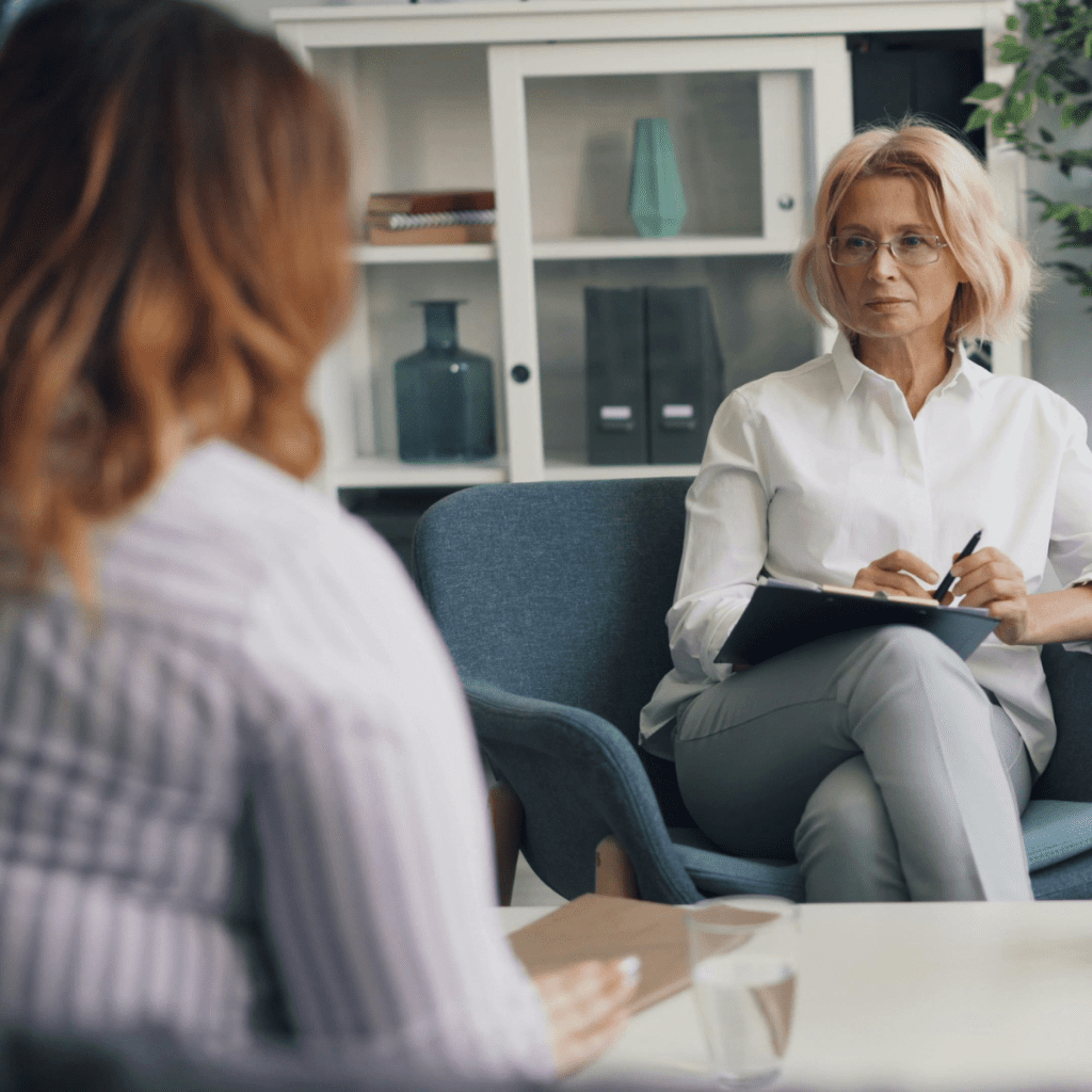 Psychologist holding notepad seated across from adult patient during a counseling session in a professional office