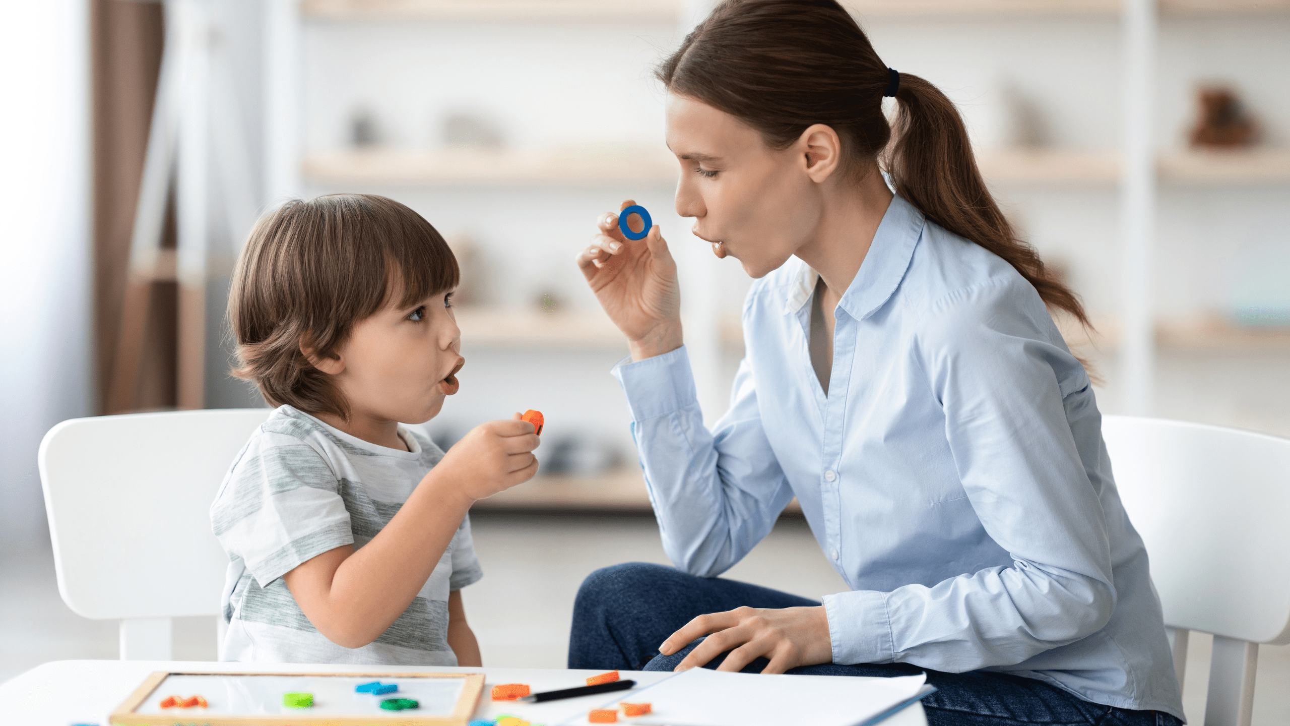 Speech language pathologist working with child on speech sounds using therapy tool during pediatric speech therapy session in clinical setting